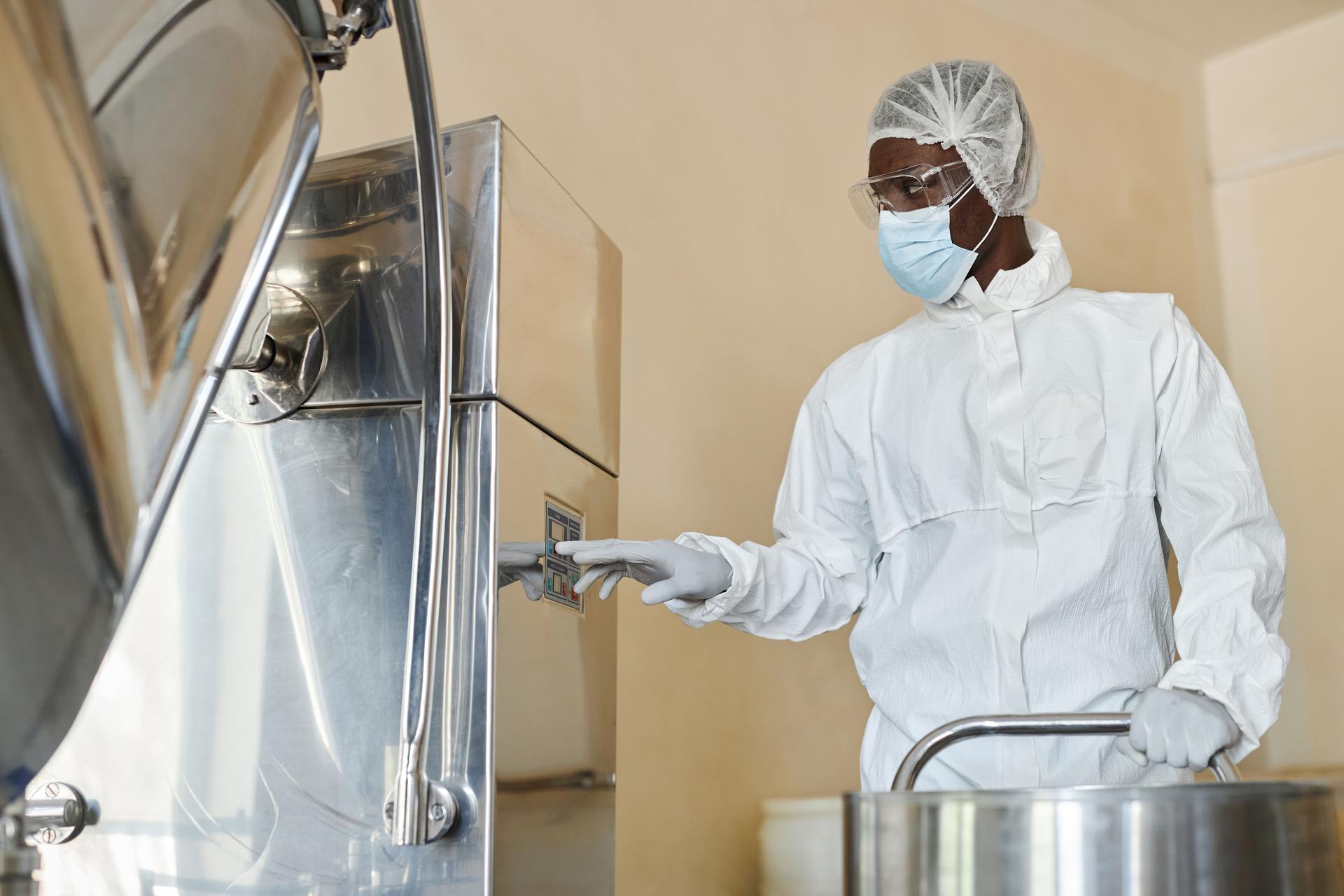 Young black man wearing protective suit operating equipment in factory workshop
